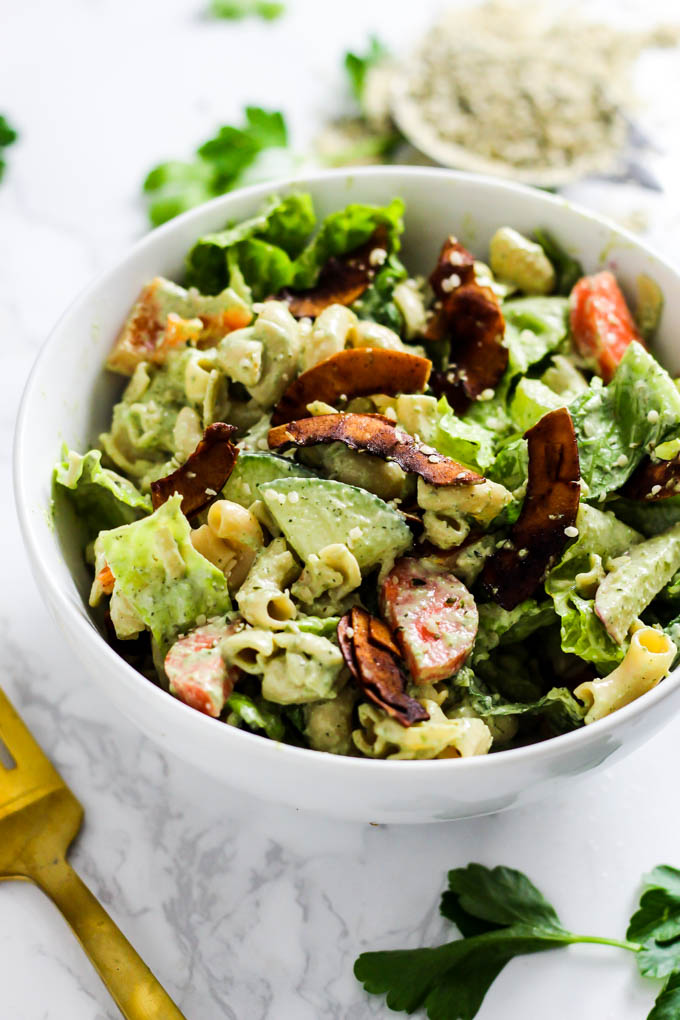 A bowl of vegan pasta salad topped with coconut bacon flakes and hemp seeds