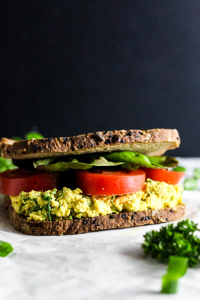 A vegan egg salad sandwich topped with tomato and lettuce