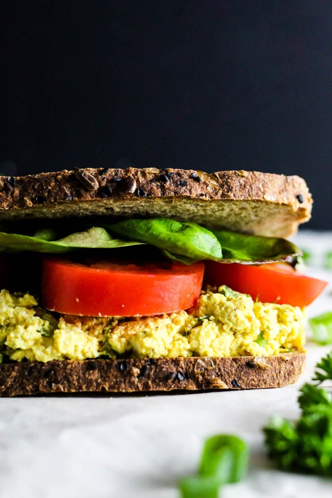 A close up of a tofu salad sandwich topped with slices of tomato and lettuce