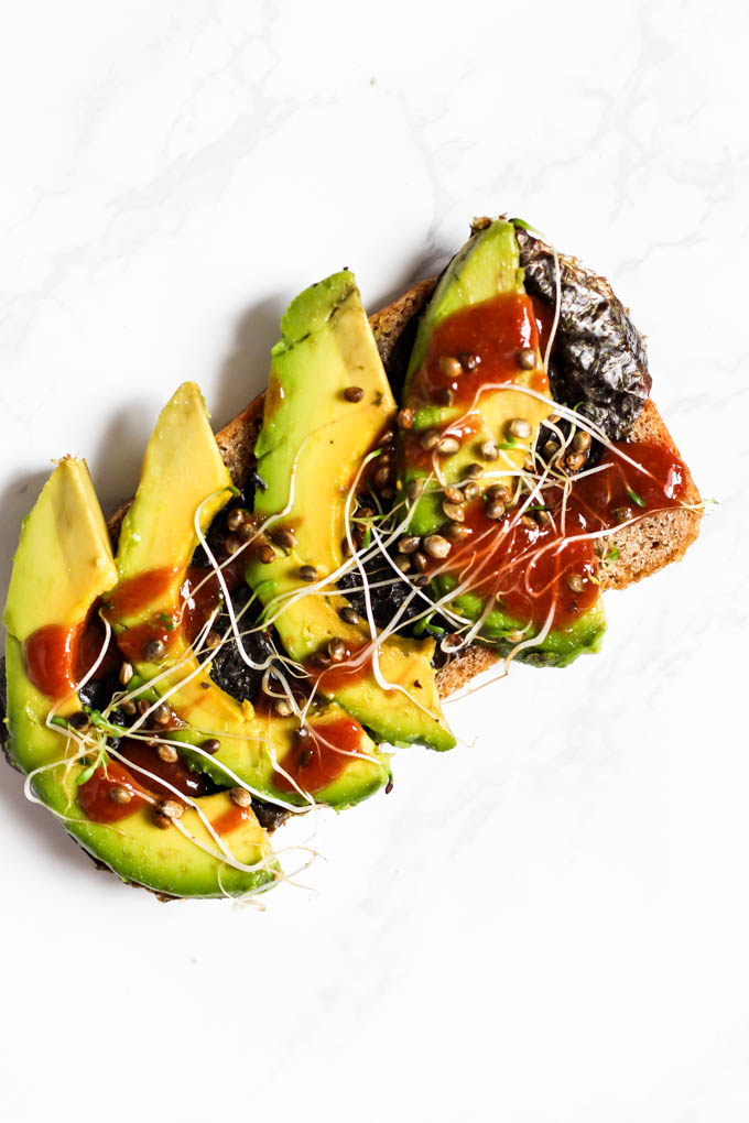 Avocado toast topped with nori, sriracha, sprouts and hemp hearts