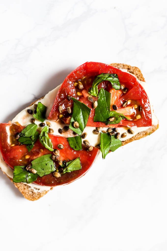 A slice of toast topped with tomatoes, fresh basil, hemp hearts and vegan cream cheese