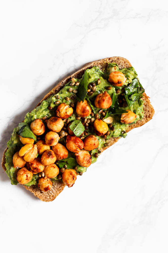 A slice of toast topped with vegan pesto, chickpeas, basil and hemp hearts