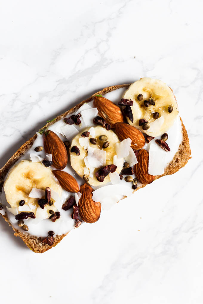 A piece of toast spread with coconut yogurt and topped with almonds, coconut, cacao nibs and sliced bananas