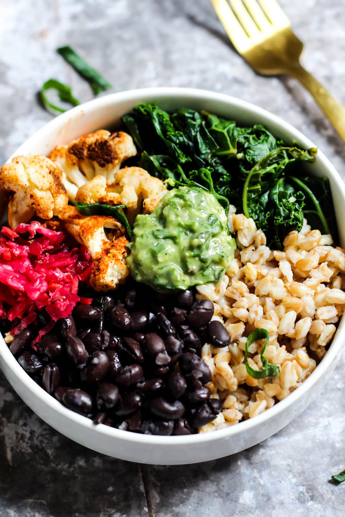 An overhead shot of a power bowl made with black beans, cauliflower, sauerkraut, farro and wilted kale