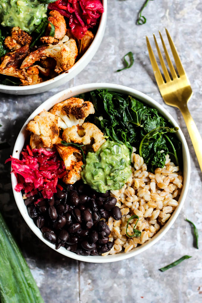 Two bowls packed with farro, black beans, sauerkraut, roasted cauliflower, wilted kale and avocado pesto