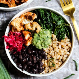 A bowl packed with farro, black beans, sauerkraut, cauliflower, wilted kale and avocado pesto