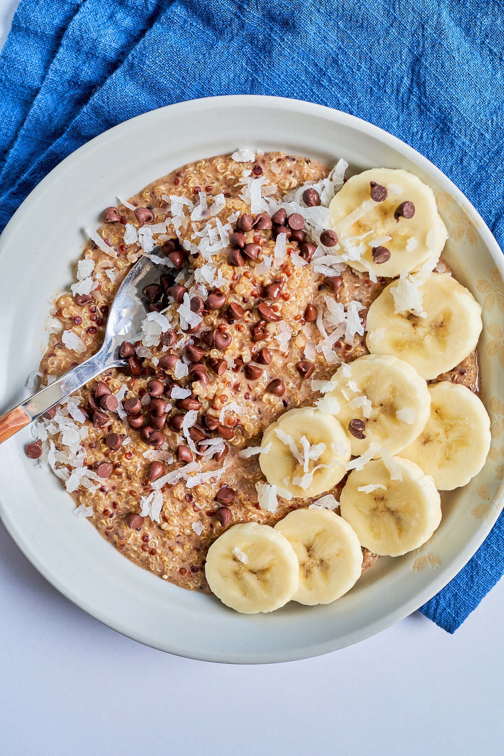 a spoon digging into a bowl of quinoa topped with shredded coconut and sliced banana