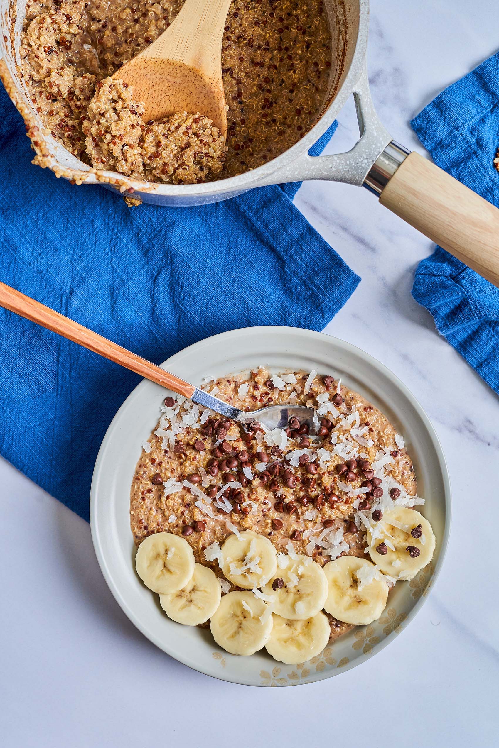 a pot of quinoa next to a bowl of quinoa porridge topped with sliced bananas and mini chocolate chips