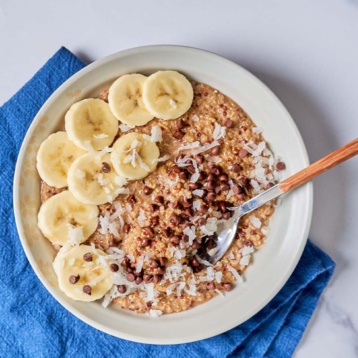 a bowl of quinoa porridge topped with bananas, coconut, and chocolate chips