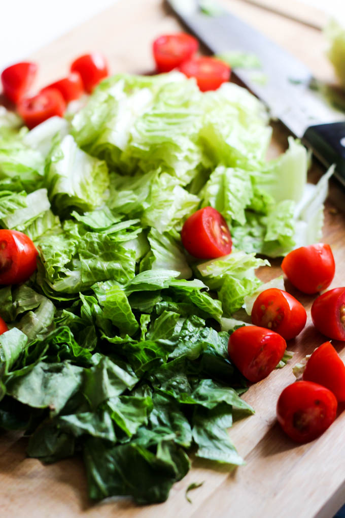 romaine lettuce and cherry tomatoes being sliced on a wooden cutting board