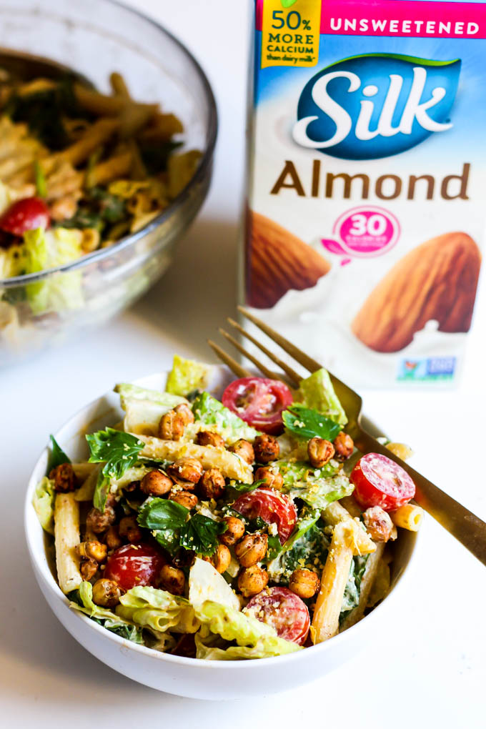 A bowl of vegan pasta salad with homemade vegan caesar dressing sits next to a carton of almond milk