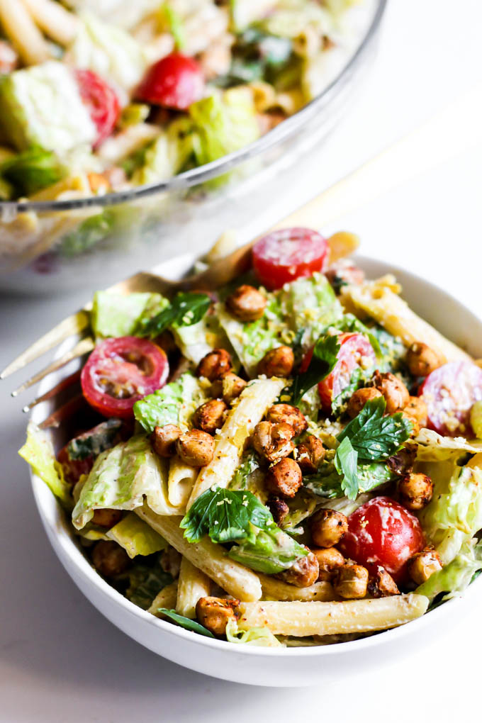 a vegan pasta salad made with homemade caesar dressing, penne pasta, romaine, parsley and chopped tomatoes topped off with roasted chickpeas