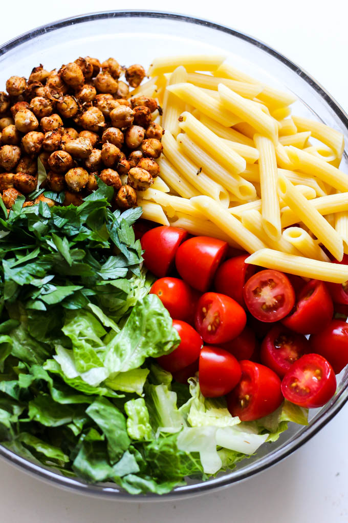 A mixing bowl filled with chopped romaine, parsley, tomatoes, roasted chickpeas and penne pasta