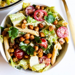 A bowl of pasta salad made with homemade vegan caesar dressing, penne pasta, lettuce, chopped cherry tomatoes, parsley and roasted chickpeas