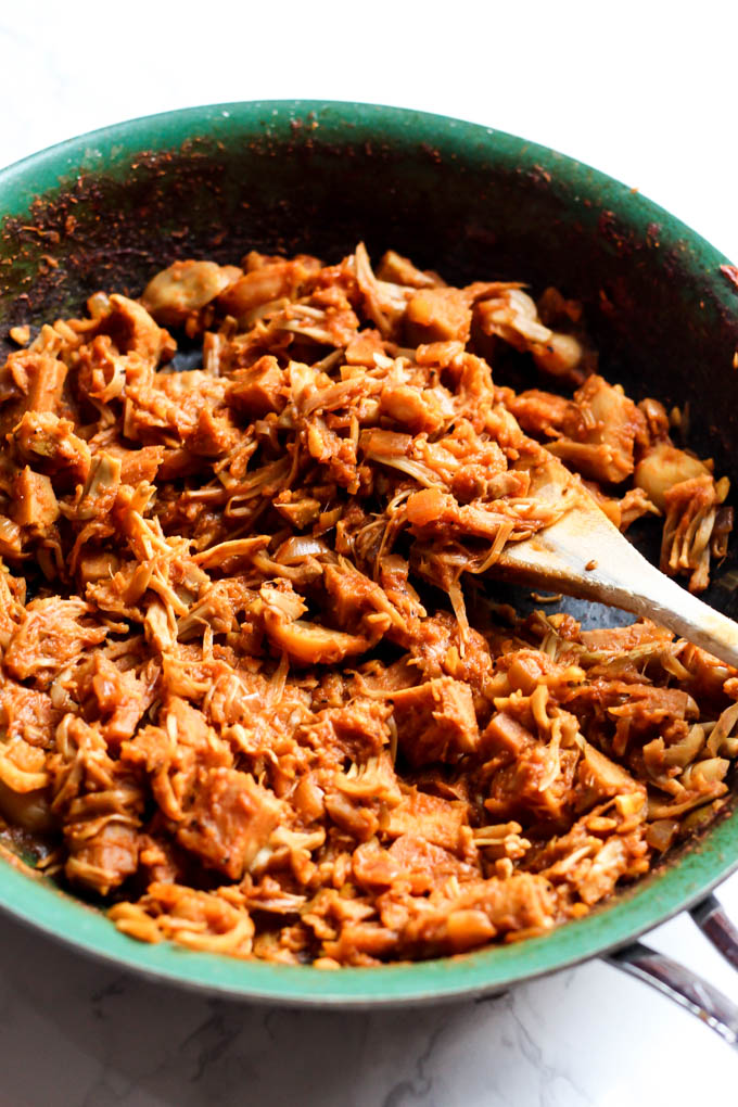 A pan of shredded bbq jackfruit being stirred with a wooden spoon