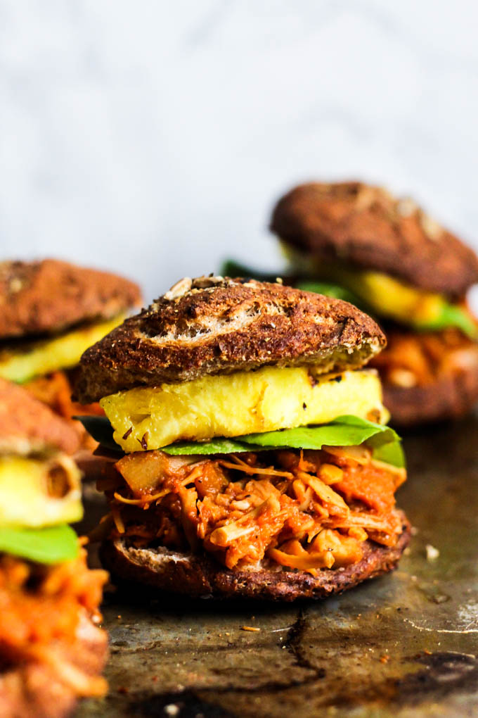 A shredded bbq jackfruit sandwich served on a pretzel bun with lettuce and pineapple