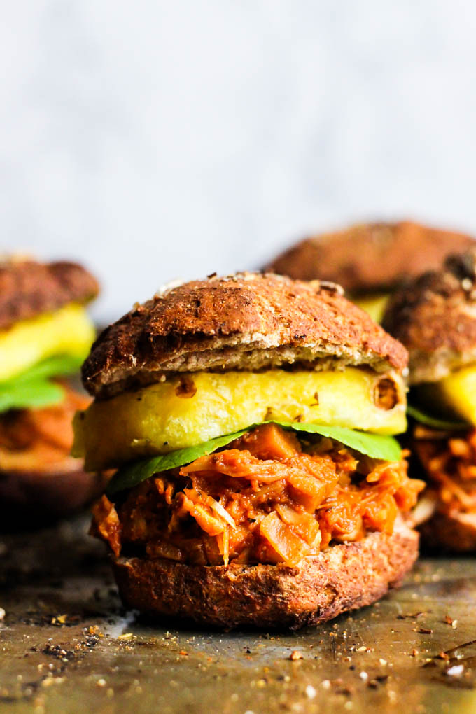 A vegan pulled pork sandwich served on a pretzel bun with pineapple and lettuce