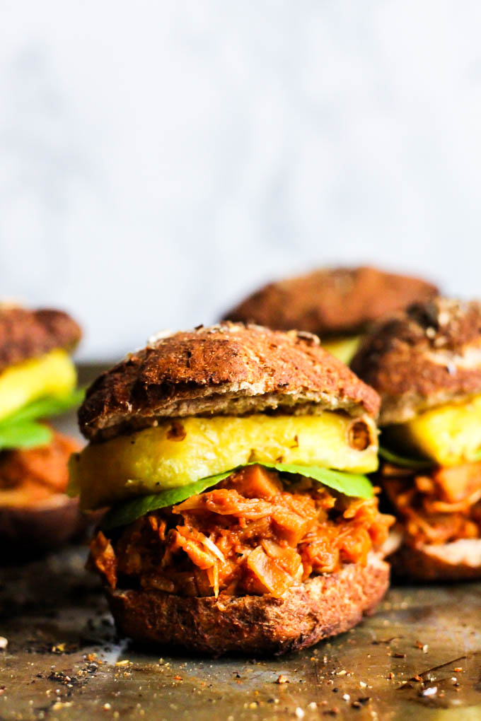 a tray of vegan pulled jackfruit sandwiches topped with slices of pineapple and lettuce