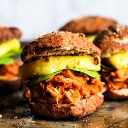 vegan pulled pork sandwiches served on a pretzel bun with a slice of pineapple