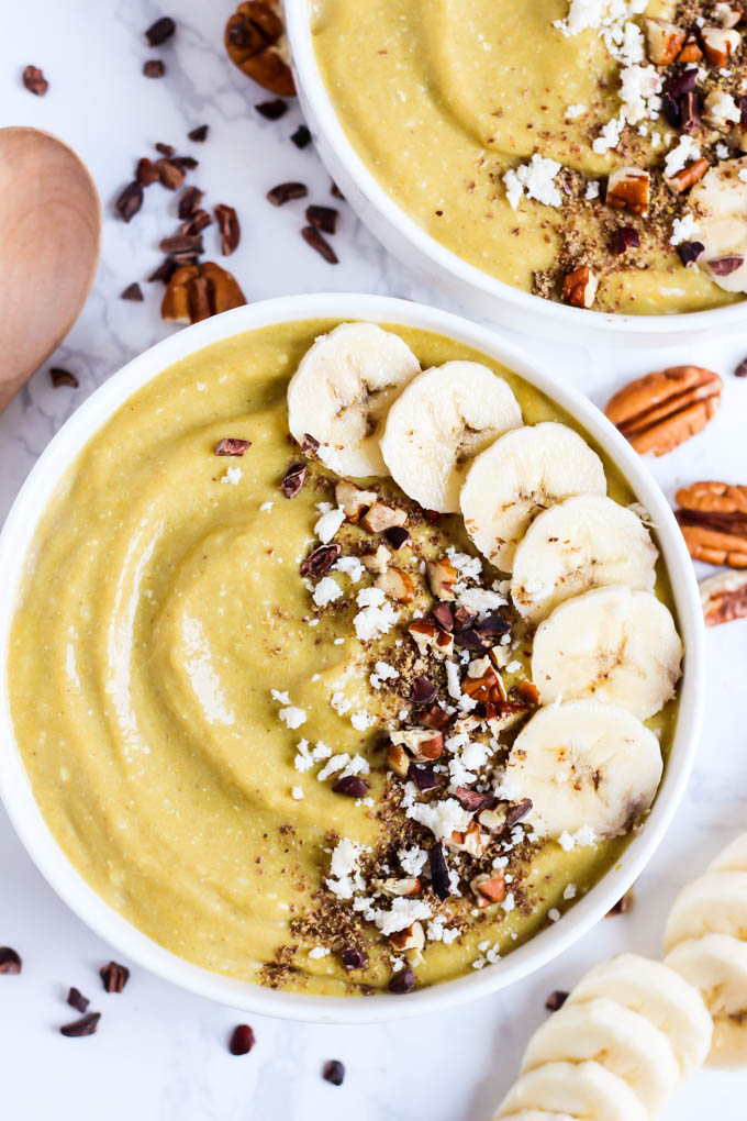 A banana smoothie bowl topped with pecans, cacao nibs, coconut and banana slices