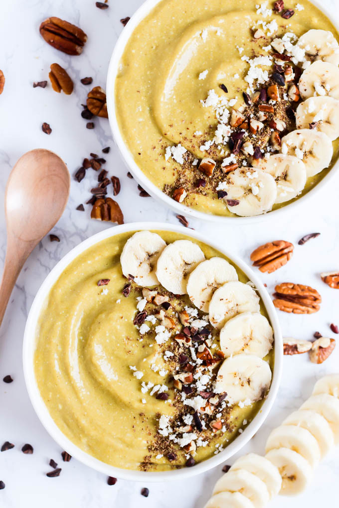 two smoothie bowls topped with bananas, pecans, chocolate and coconut