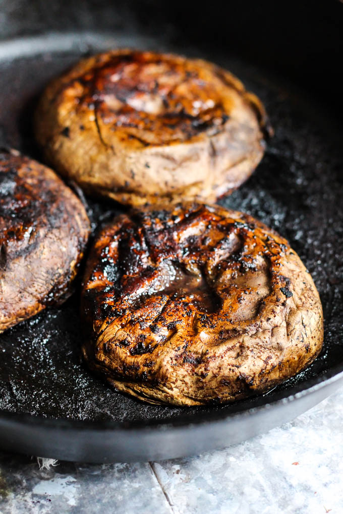 three portobello mushroom caps being seared in a cast iron skillet