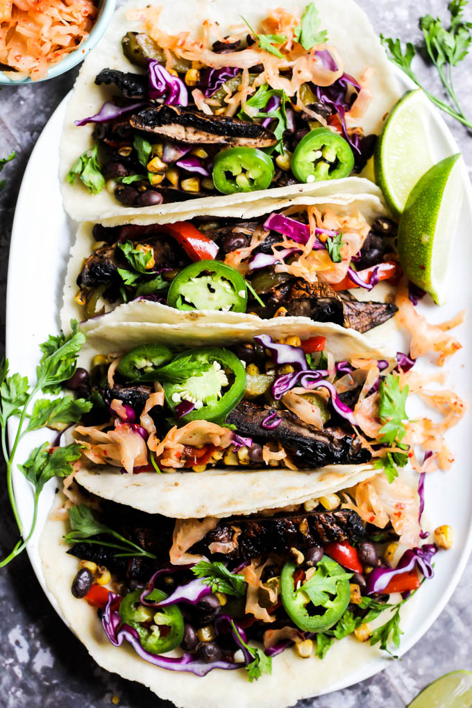 an overhead shot of a platter of portobello mushroom tacos topped with cilantro, jalapenos and served with lime slices