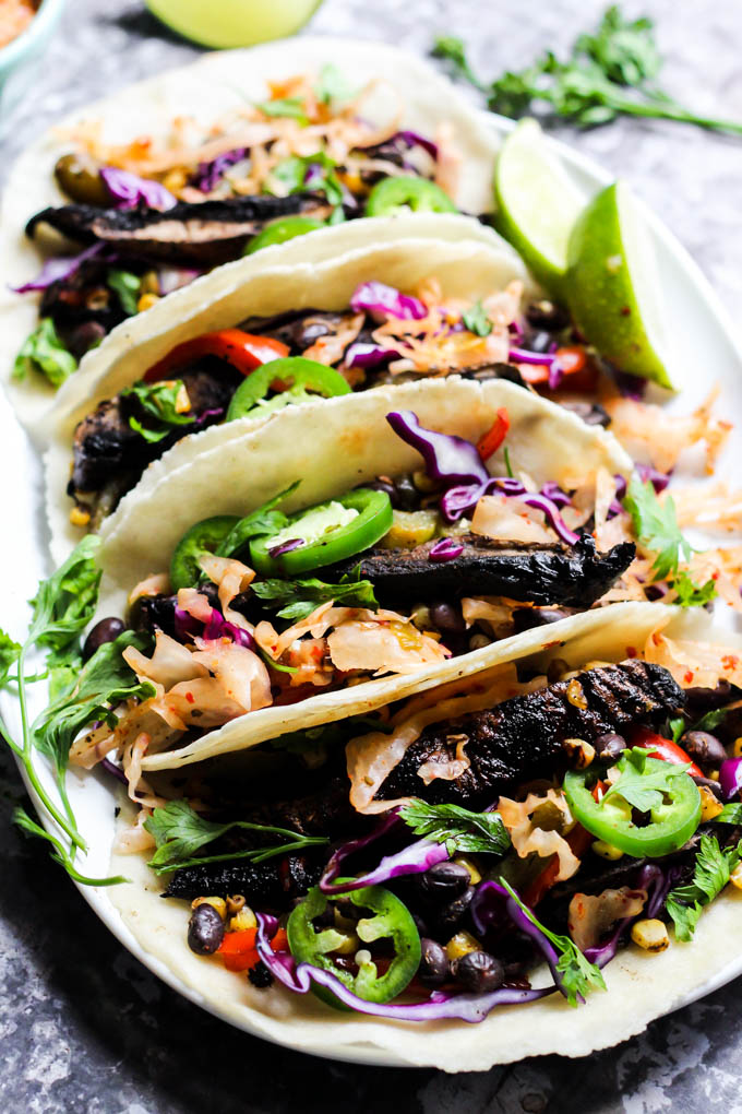 four vegan mushroom tacos plated on a white platter alongside lime wedges