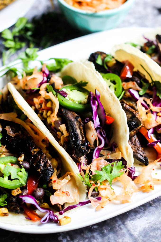 a white serving platter with three mushroom tacos topped with cabbage and jalapenos