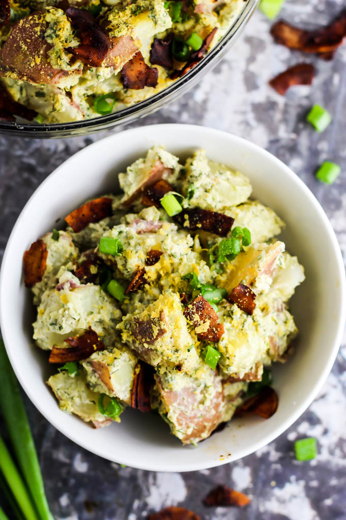 a bowl of vegan bacon ranch potato salad surrounded by green onions and coconut bacon flakes