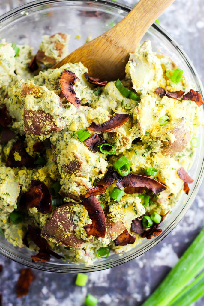 a large bowl of vegan bacon ranch potato salad being stirred with a wooden spoon