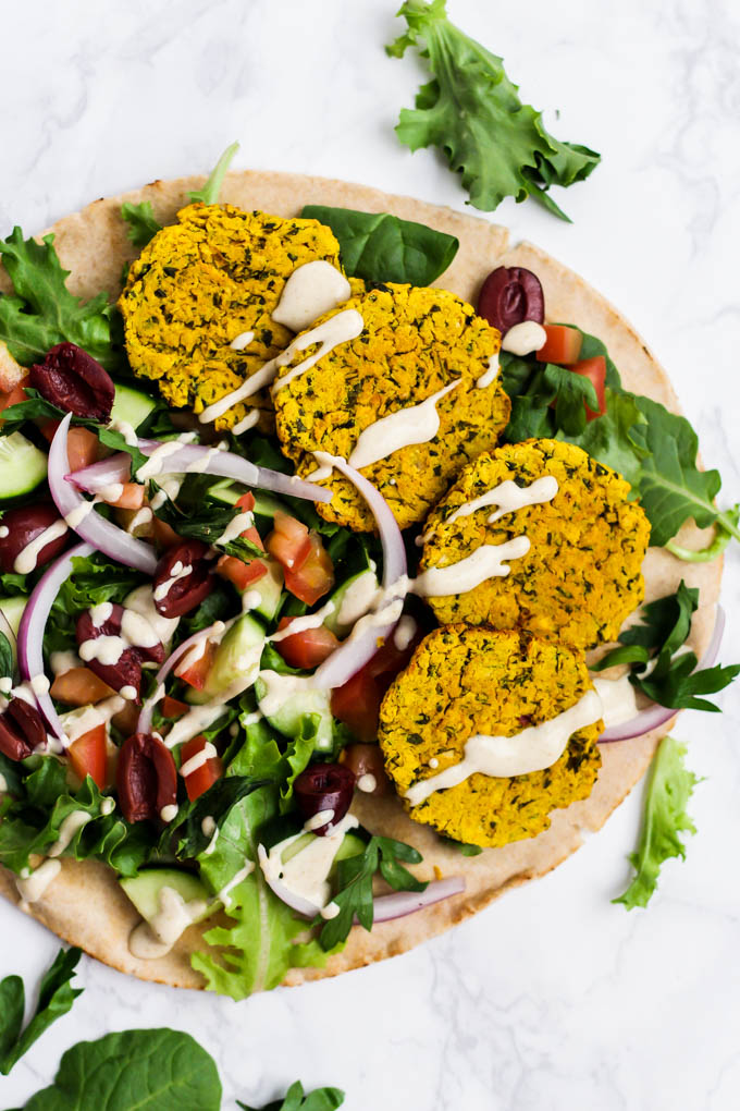 an openfaced pita sandwiched with 4 falafels, veggies, greens and tahini