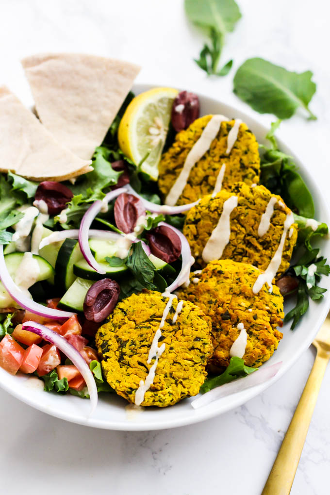 a falafel bowl served with pita bread, greens, veggies and tahini sauce