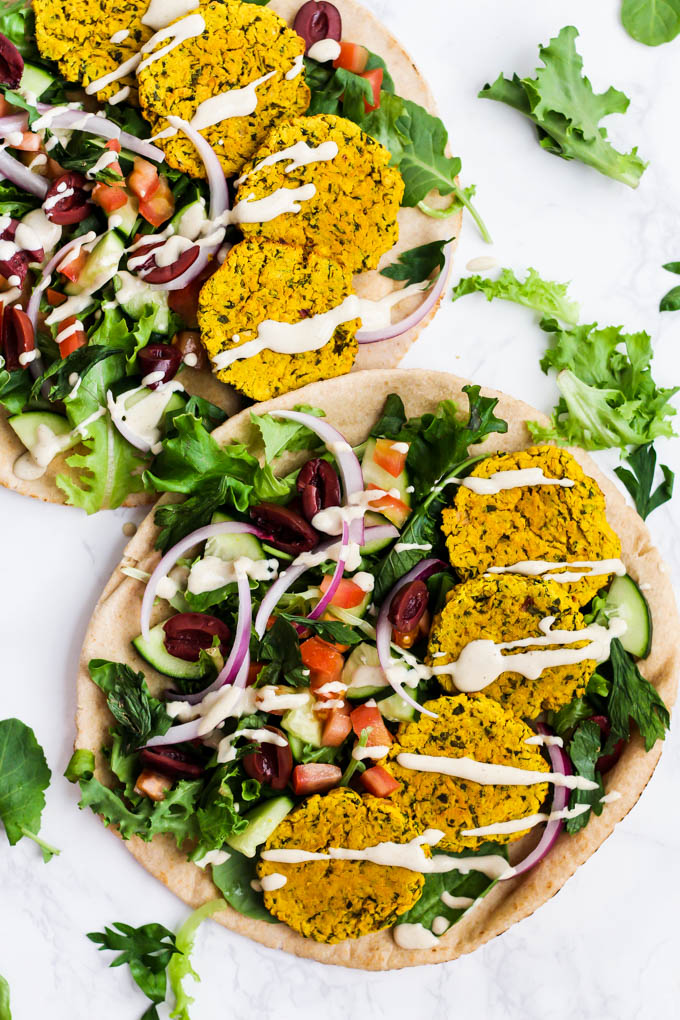 two pieces of pita bread, each topped with falafel, greens, cucumbers, tomatoes, olives and red onion