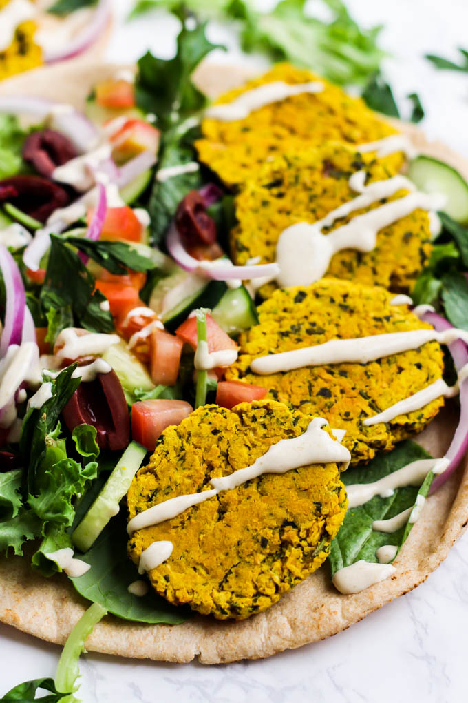 a close up of a pita topped with four turmeric falafels with veggies and tahini