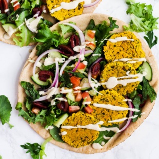 four turmeric falafels served in a pita with greens, tomatoes, cucumber, olives, red onion, and a tahini drizzle