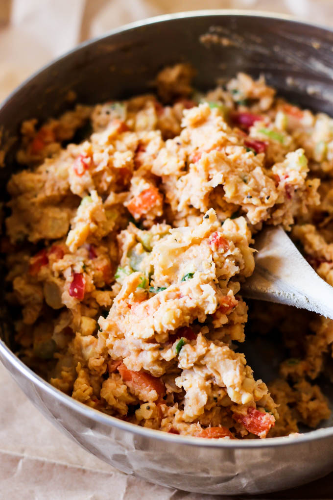 A large mixing bowl of buffalo chickpea salad being mixed with a wooden spoon