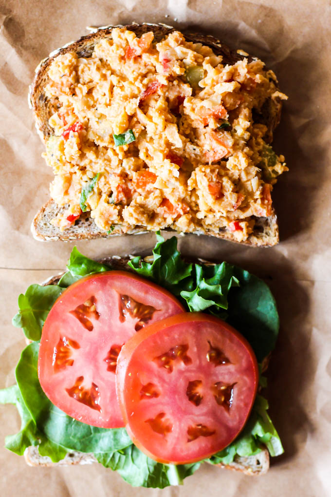 Two slices of sprouted bread, one half topped with a chickpea salad and the other half topped with lettuce and two slices of tomato