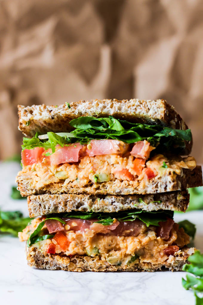 a buffalo chickpea salad is served as a sandwich with whole grain sprouted bread, lettuce and tomatoes