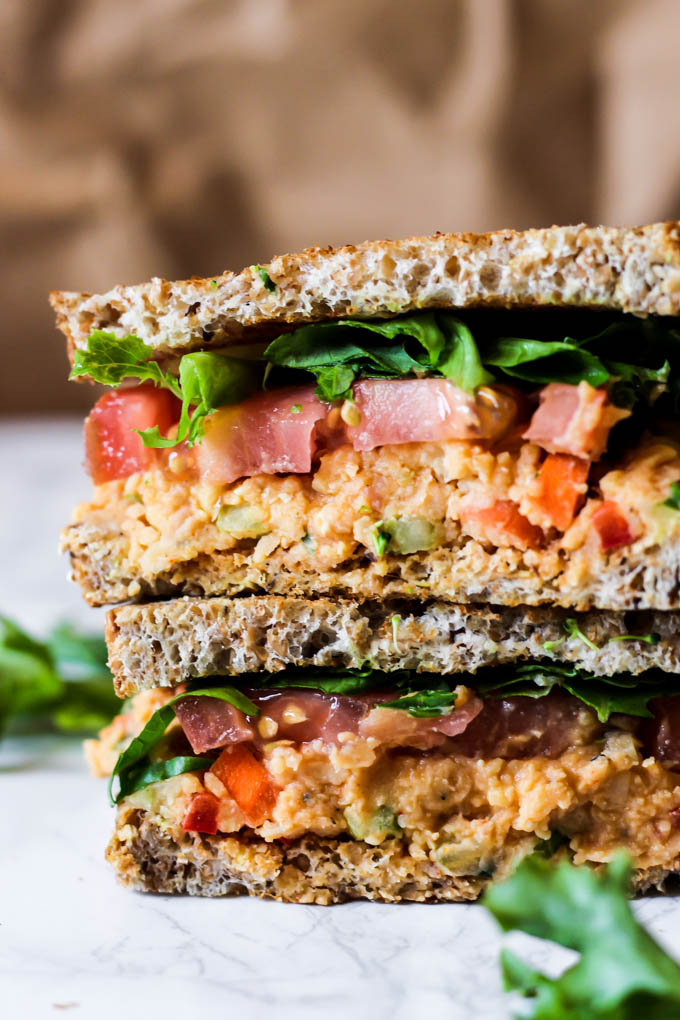 Two halves of a chickpea salad sandwich topped with lettuce and tomato slices