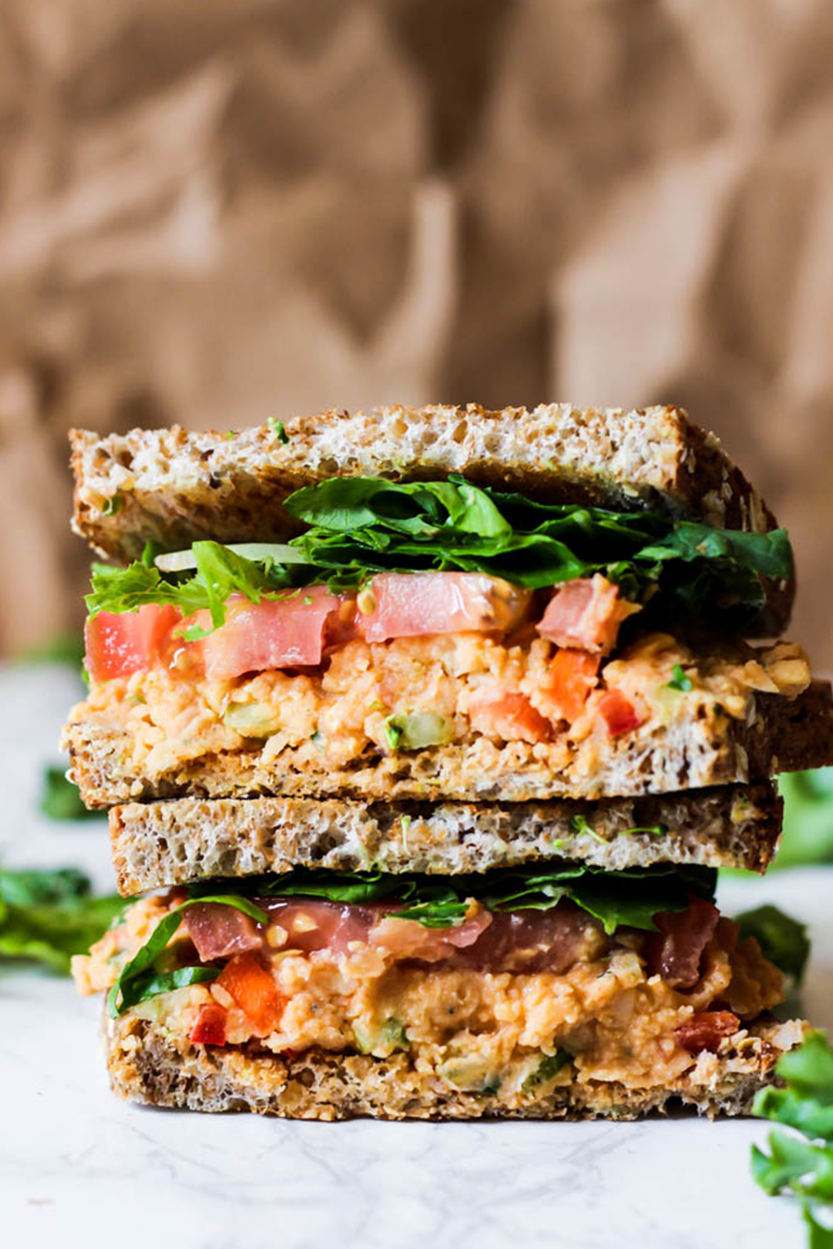 a buffalo chickpea salad sandwich served with greens and sliced tomatoes