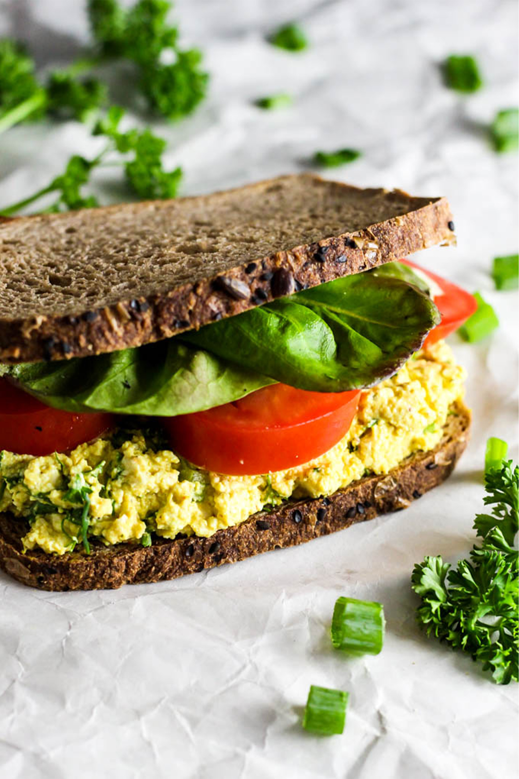 a vegan egg salad sandwich served on wheat bread with spinach and sliced tomatoes