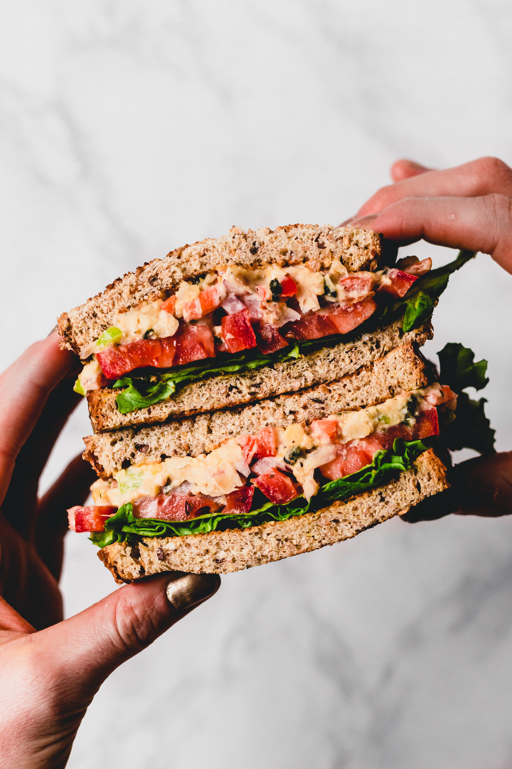 two hands holding two halves of a vegan tuna salad sandwich