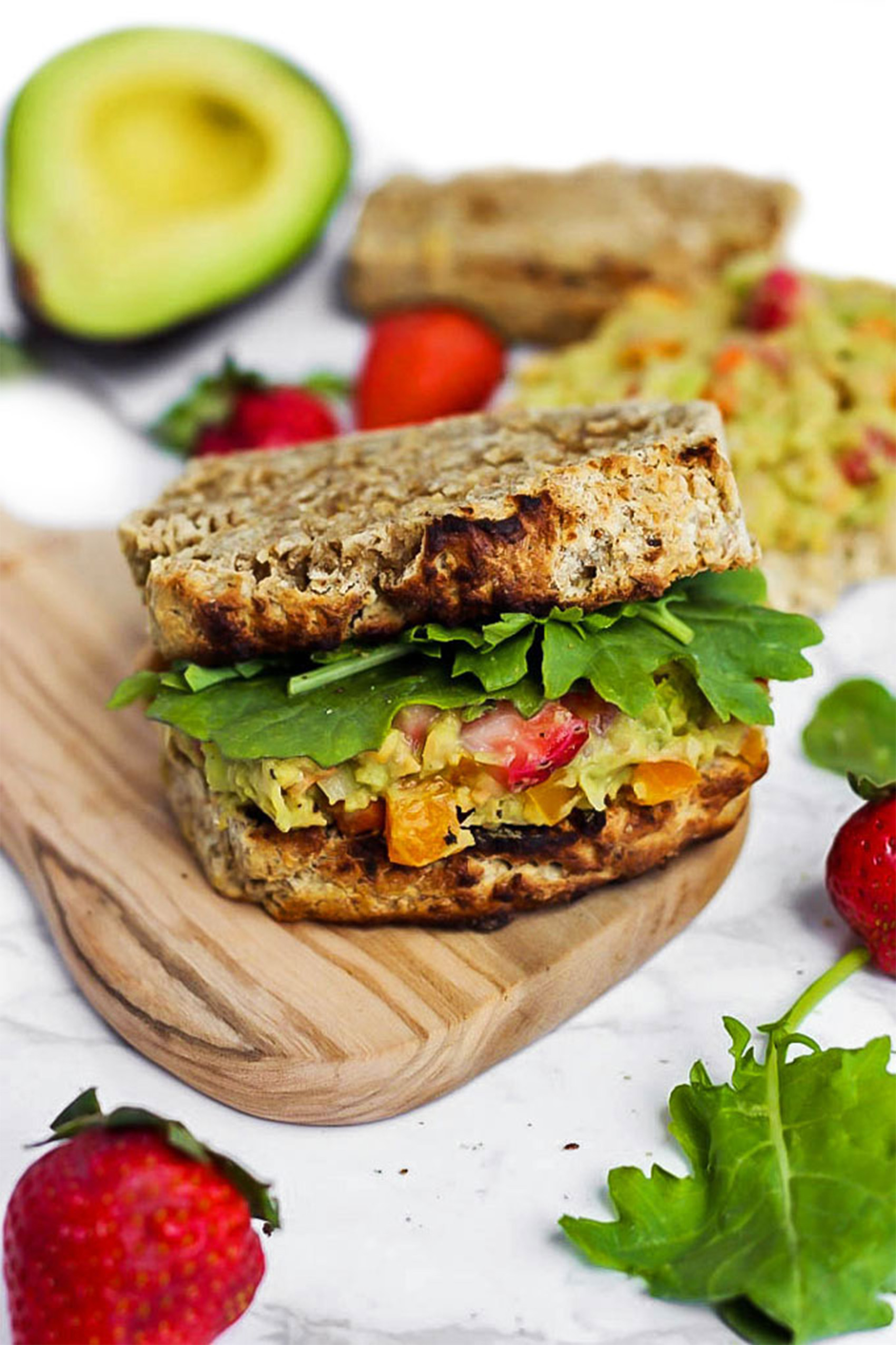 a strawberry chickpea salad sandwich served on a wooden platter