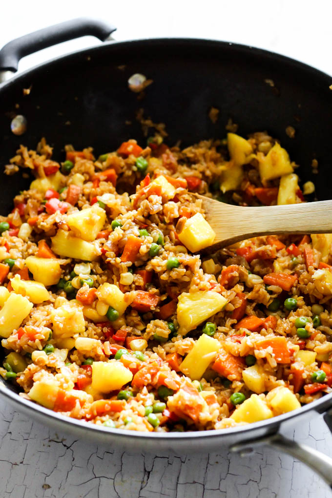 A skillet of fried rice being stirred with a wooden spoon