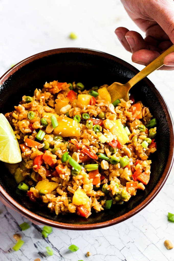 a hand with a fork taking a scoop out of a bowl of fried rice served with a wedge of lime