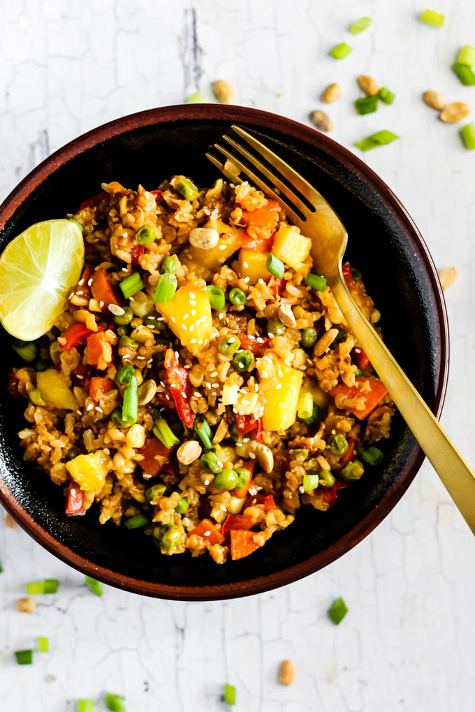 a bowl of fried rice served with a slice of lime and surrounded by chopped green onion and peanuts