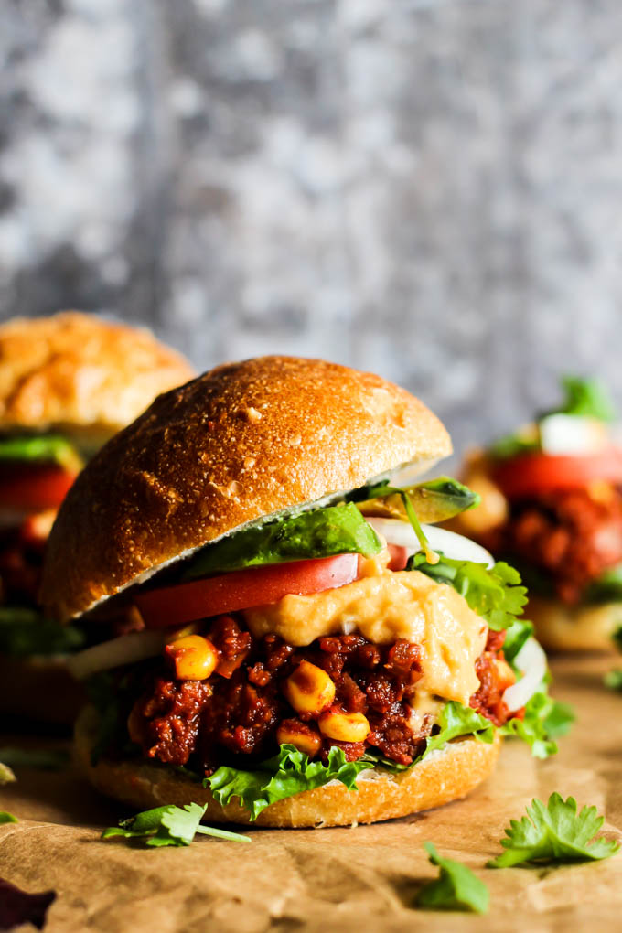 a vegan slider topped with lettuce, onion, tomato and vegan cheese sauce