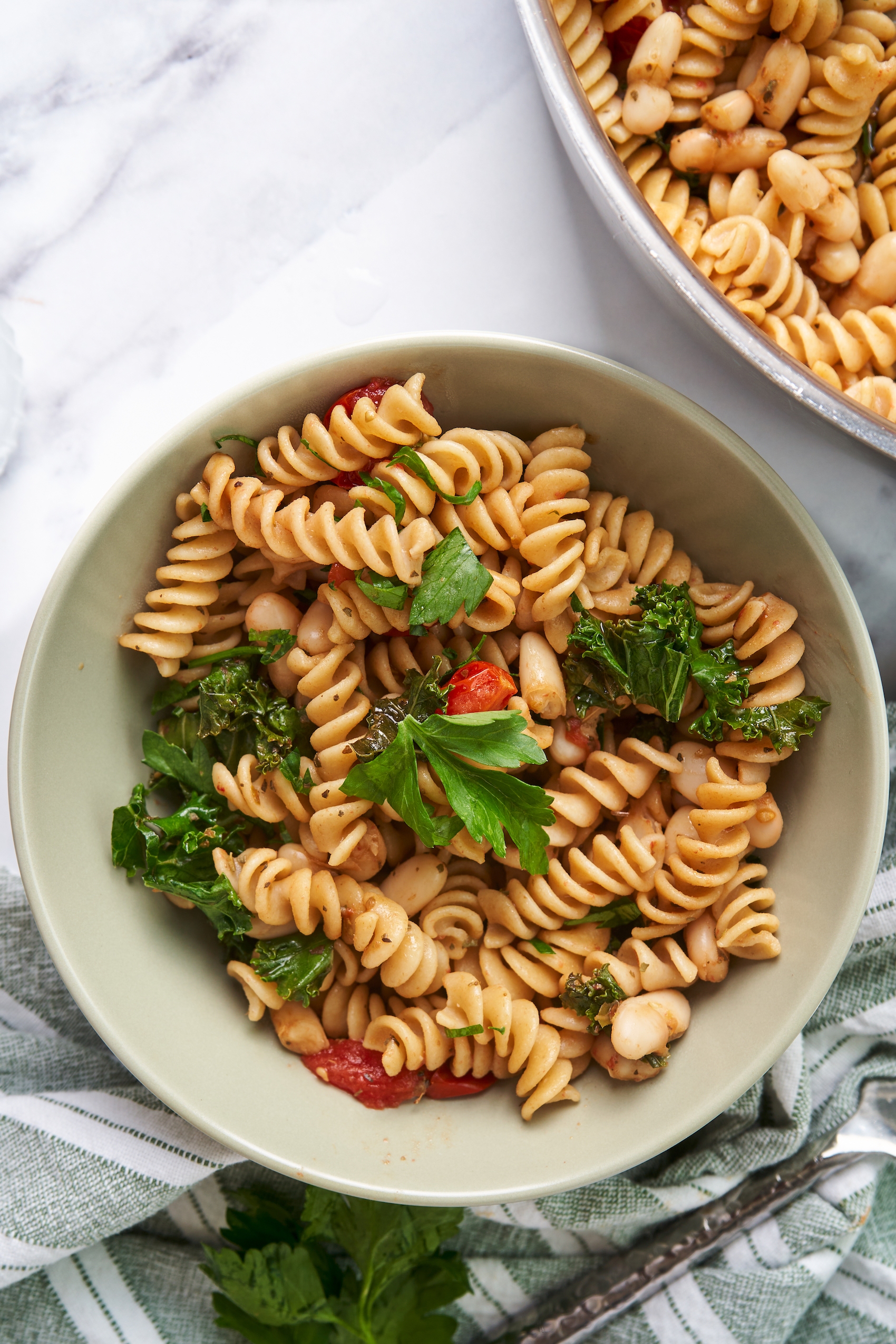 a bowl of fusilli pasta topped with parsley and served with cherry tomatoes, kale and white beans