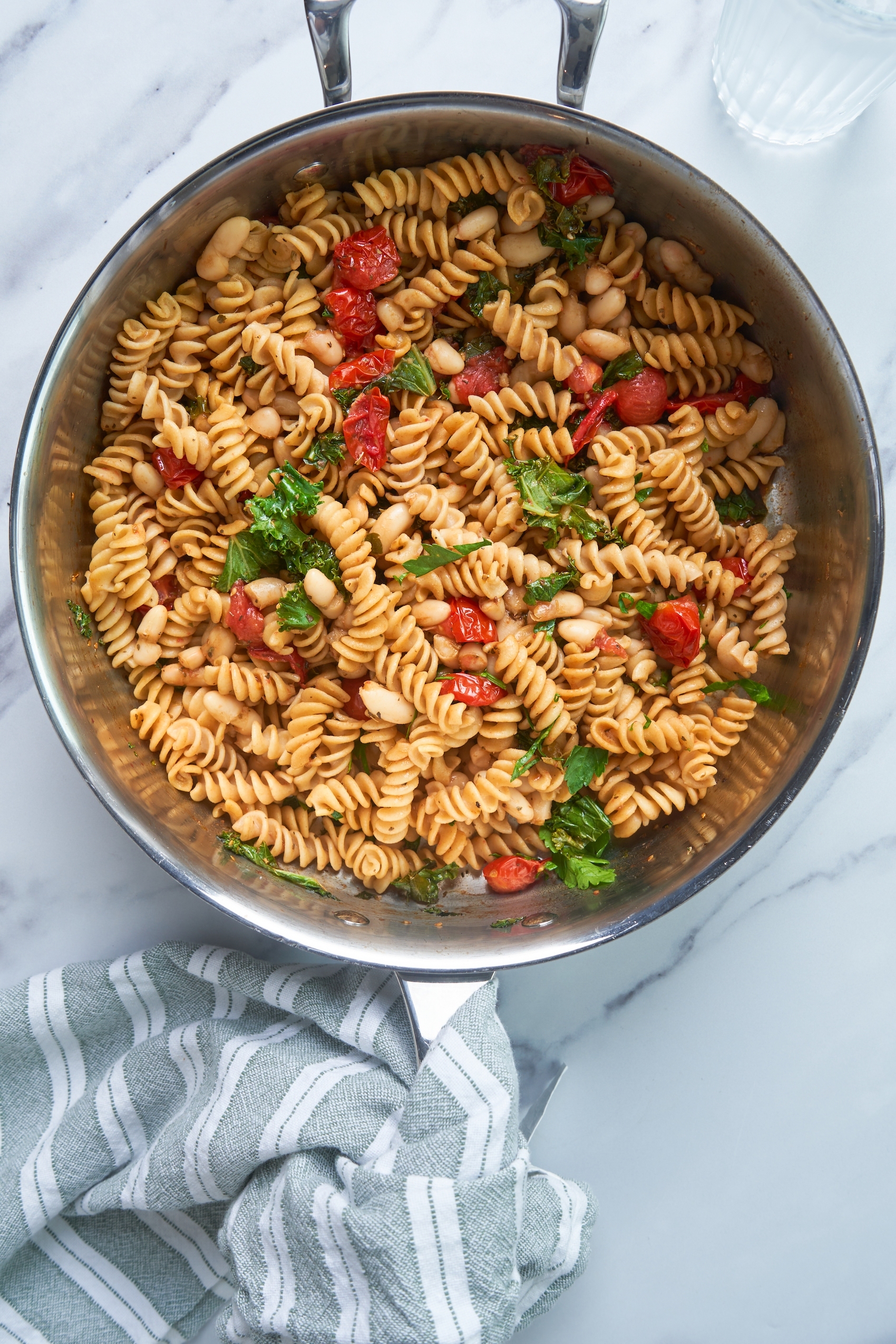 a pot filled with fusilli pasta mixed with kale, cherry tomatoes and white beans